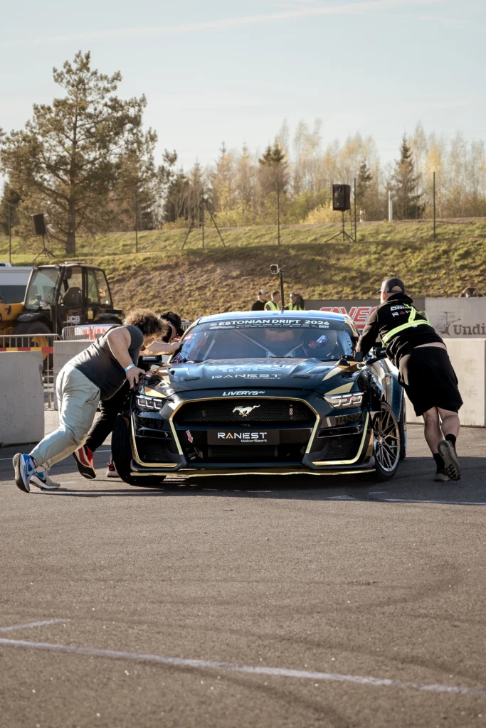 Front view of people pushing a black racing car through the paddock.