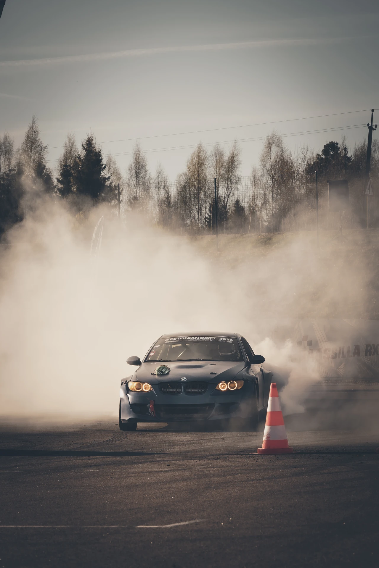 Black drift car approaching through a curtain of smoke.
