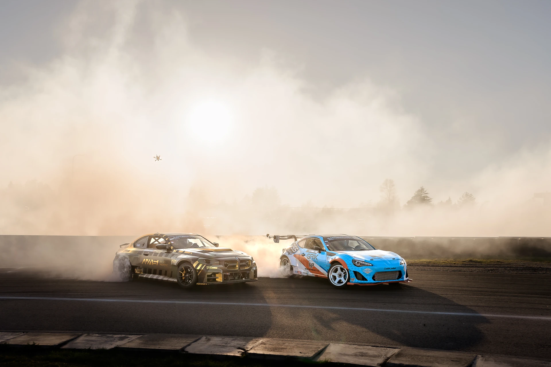 Blue and black tandem drift cars in bright backlight and smoke.