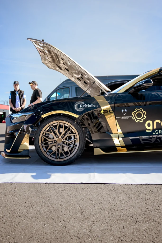 Side view of a black-and-gold racing car's open bonnet and front wheel.