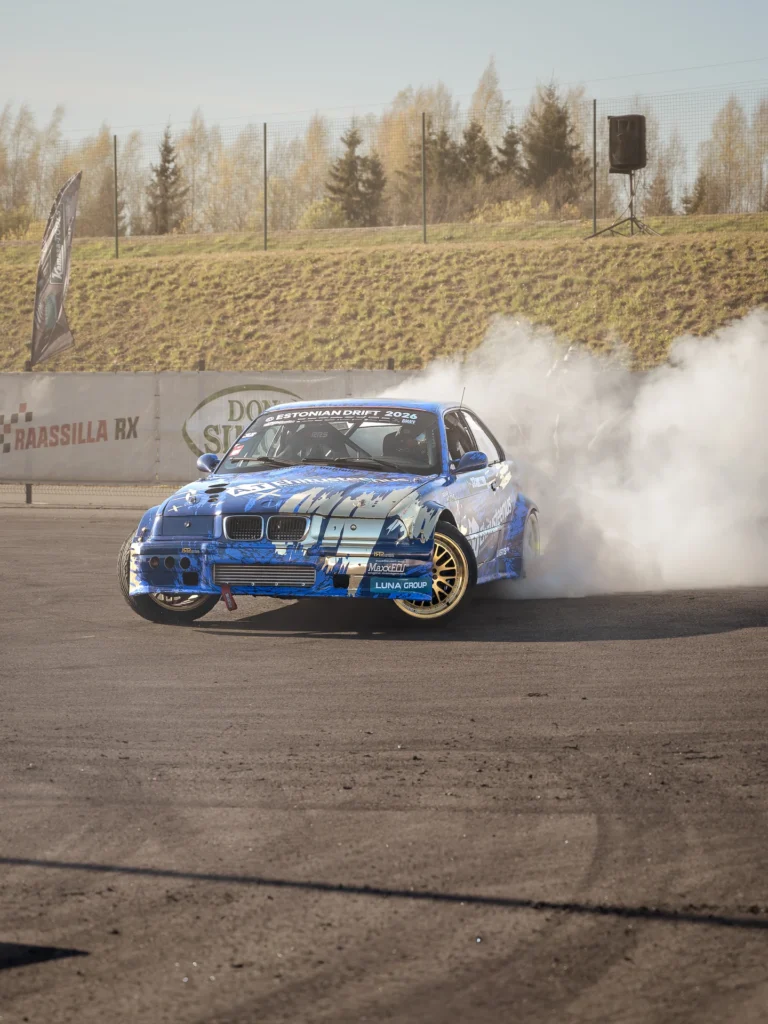 A blue drift car with gold wheels in a smoky corner, its front wheels turned sideways.