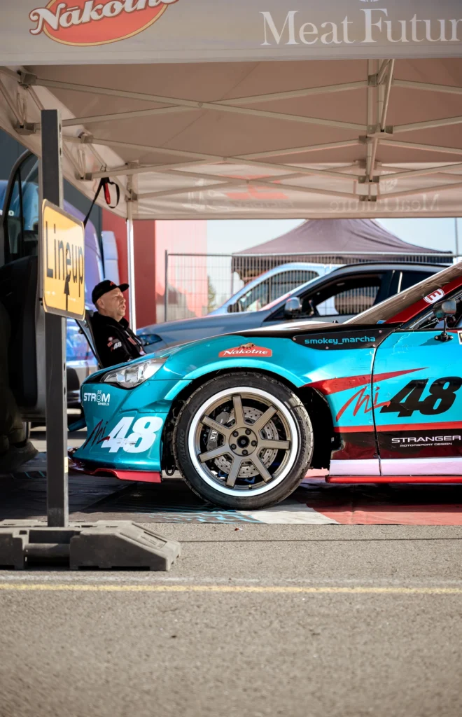 A turquoise-and-red racing car carrying number 48 stands beneath a tent.