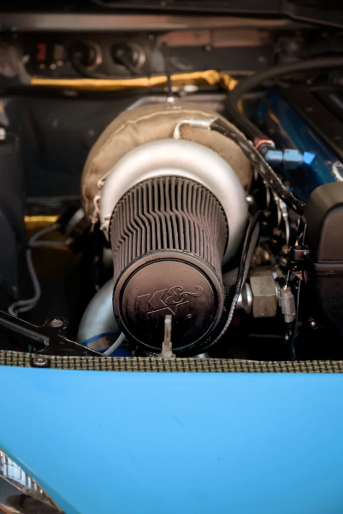 A large turbocharger and dark cone-shaped air filter in a blue car's engine bay.