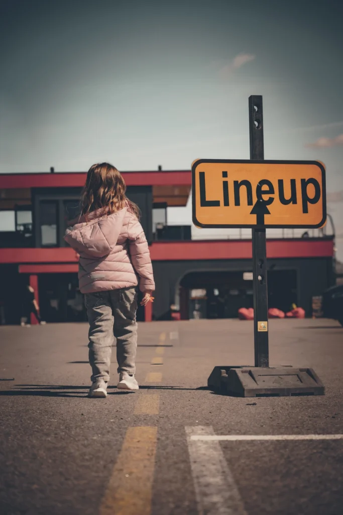 A child in a pink jacket stands facing away from the camera beside a yellow Lineup sign.
