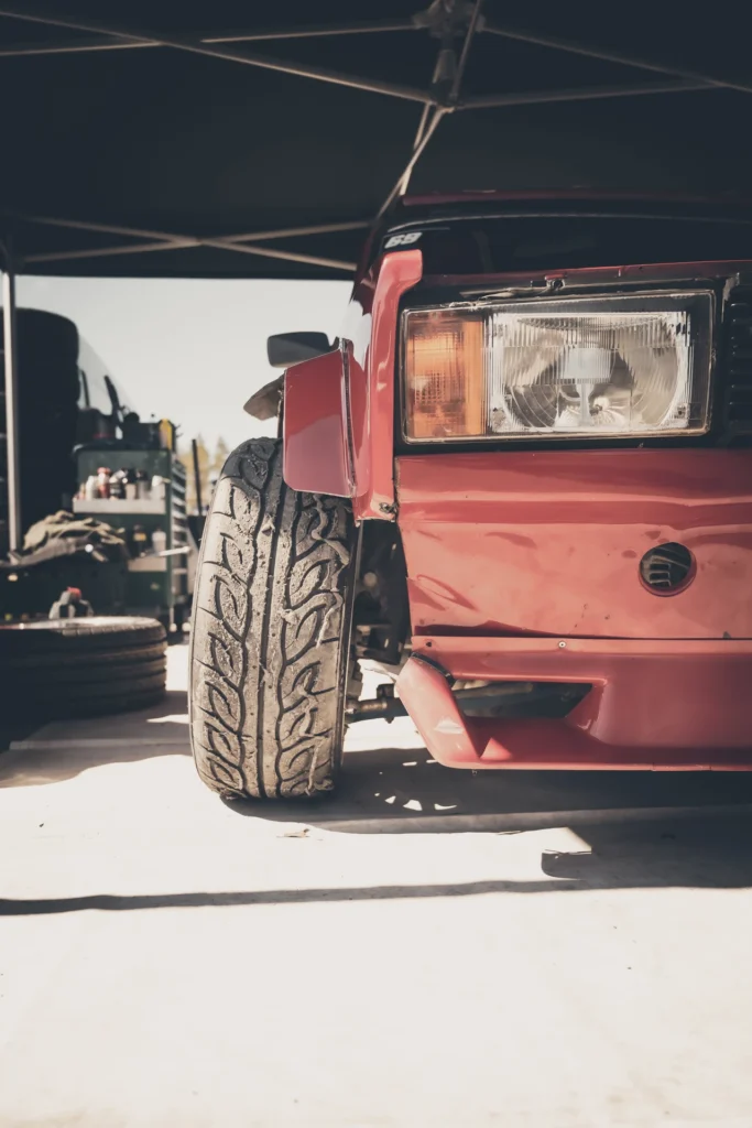 Close-up of a red car's rectangular headlight and outward-turned front wheel.