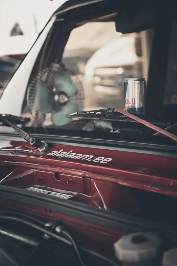 A drink can in front of a red car's windscreen, with the open engine bay in the foreground.