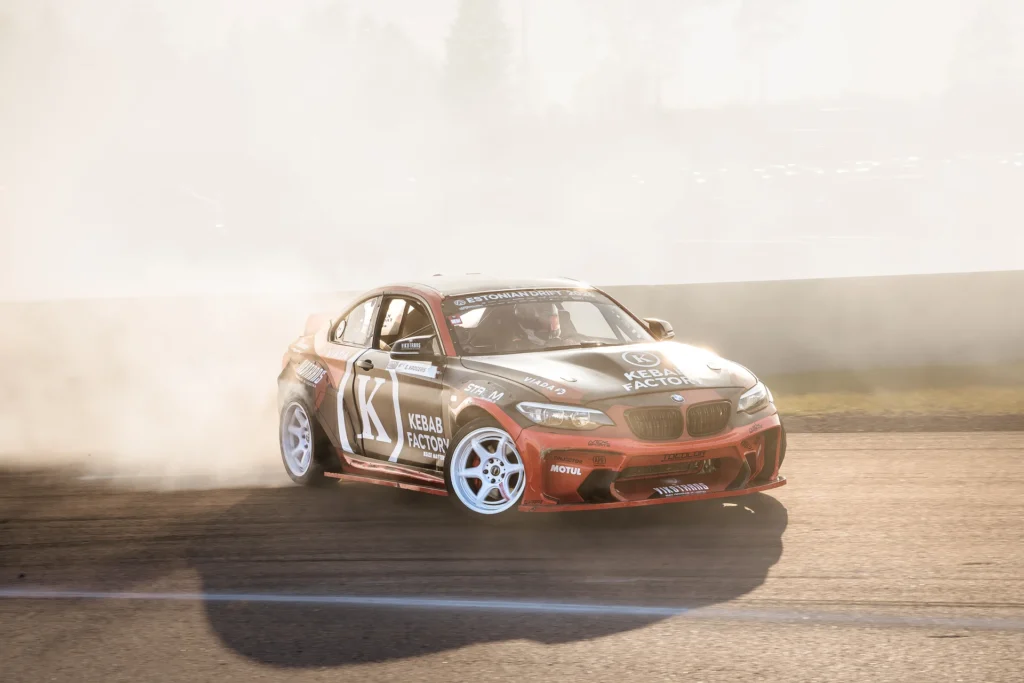 A close view of a red drift car with white wheels against a bright cloud of smoke.