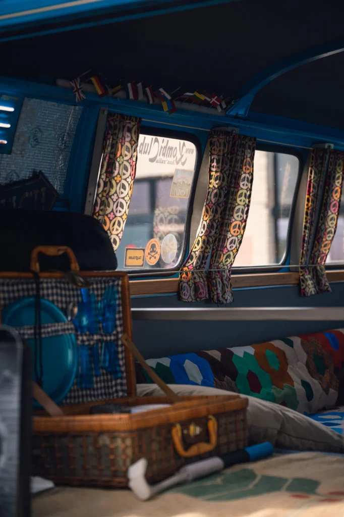 Blue campervan interior with patterned curtains, miniature flags and an open picnic basket.