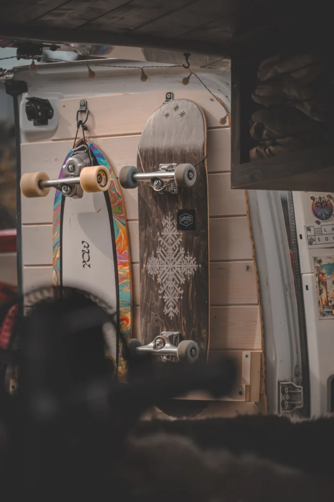 Two skateboards are mounted on the light wood-lined inside of a campervan's rear door.