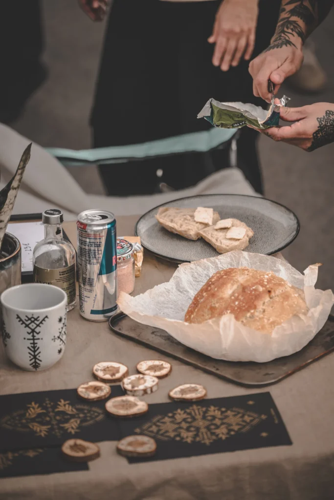 Hands prepare sandwiches at a table with a round loaf, a plate and a mug.