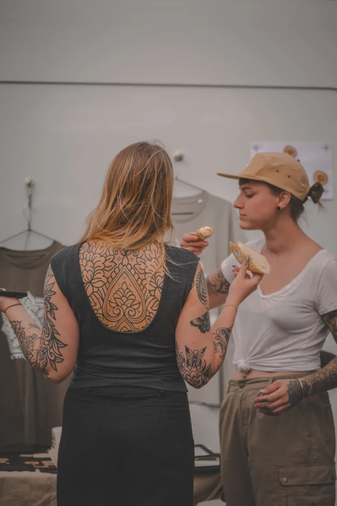 Two tattooed women stand beside a campervan, each holding a slice of bread.