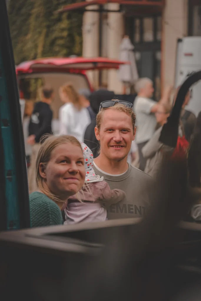 Two adults and a small child look into a campervan through an open window.