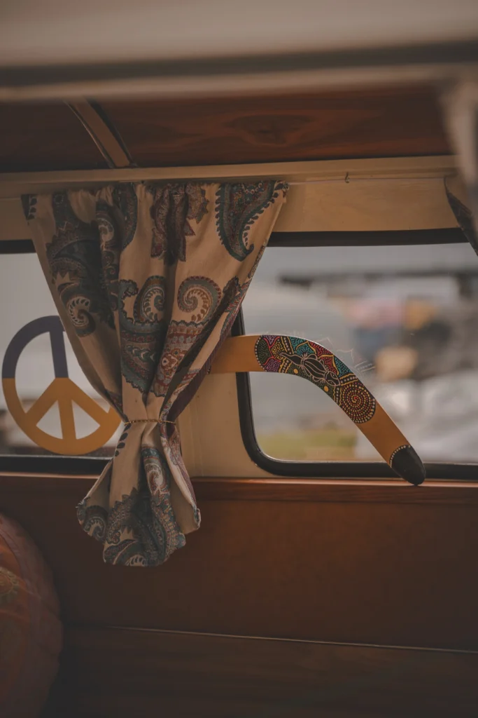 A paisley curtain, a peace sign and a colourfully decorated boomerang hang by a campervan window.