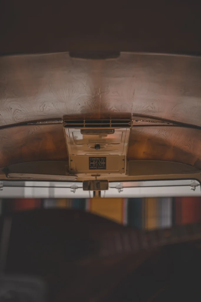 A curved wood-grain ceiling and ventilation grille above a campervan's windscreen.