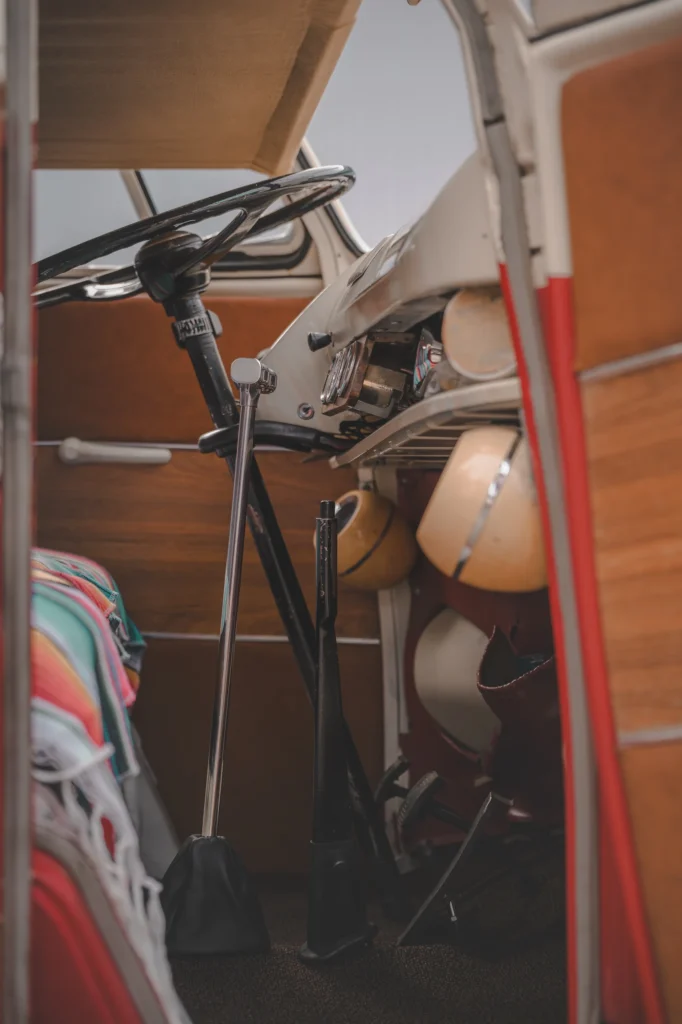 A campervan driving position with a large black steering wheel, a long gear lever and wooden door trim.