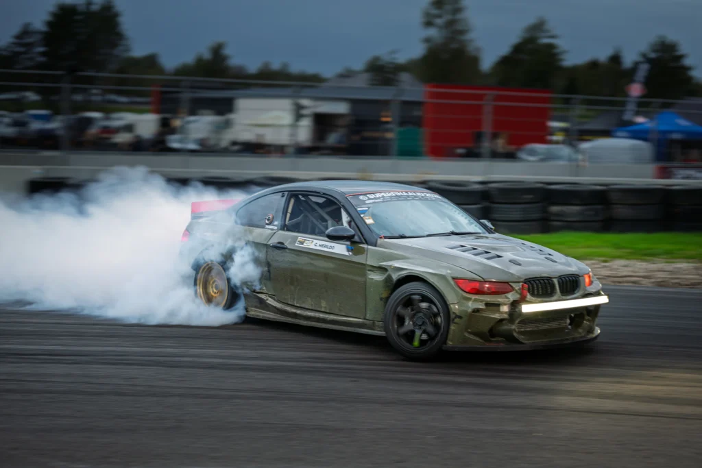 Oliivroheline BMW pööratud esiratastega külglibisemises, hall suits ja hägustunud rada taustal.