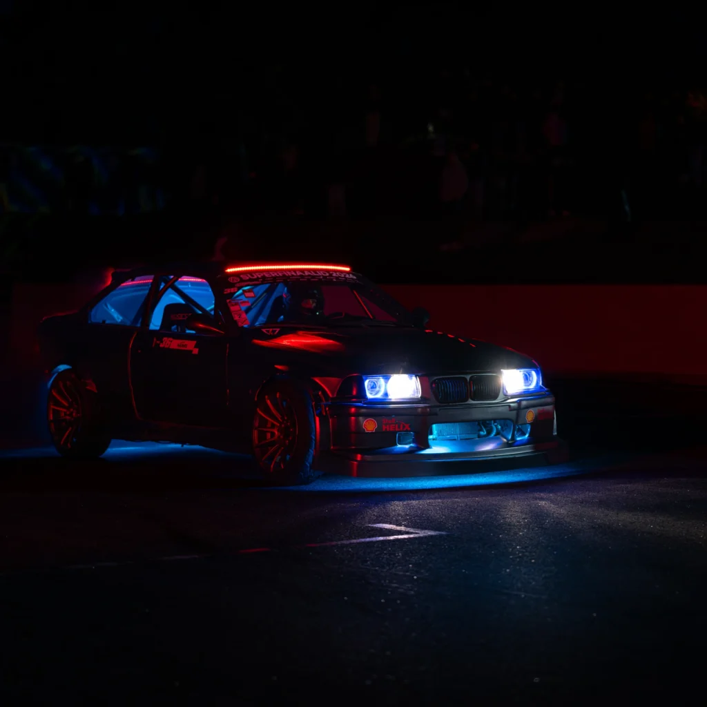 Tume BMW valgesiniste esituledega pimedal rajal, punane ja sinine valgus peegeldumas kerelt.