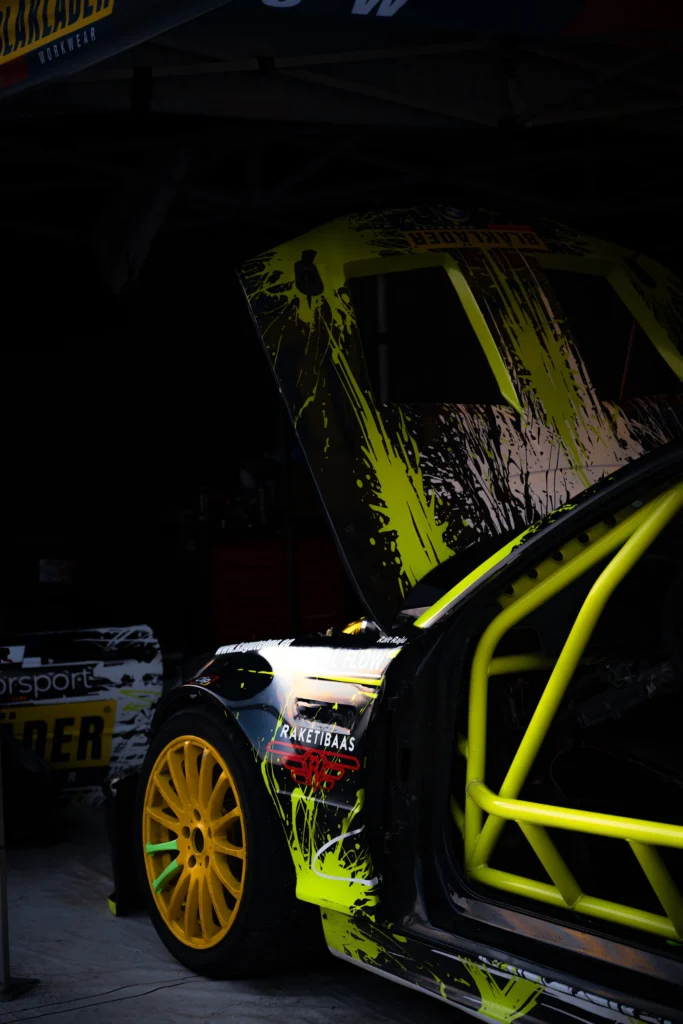 Driftiauto kollane turvapuur ja kollane velg hämaras boksis, kapott üles tõstetud.