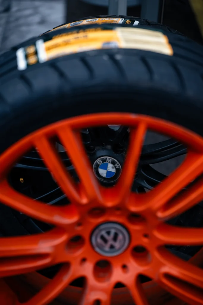 Oranži Volkswageni märgiga velje kodarate vahelt paistab must BMW velg; rehvidel on tootesildid.