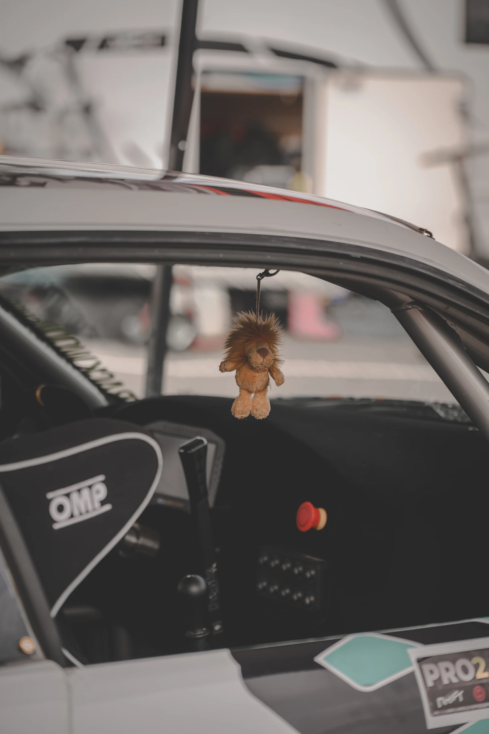 A small stuffed lion hangs inside a race car between a black bucket seat and the dashboard.