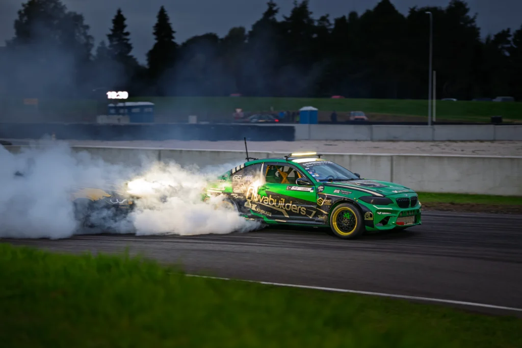 Roheline driftiauto sõidab hämaras, ere valgus peegeldumas tagaratta ümber keerlevas suitsus.