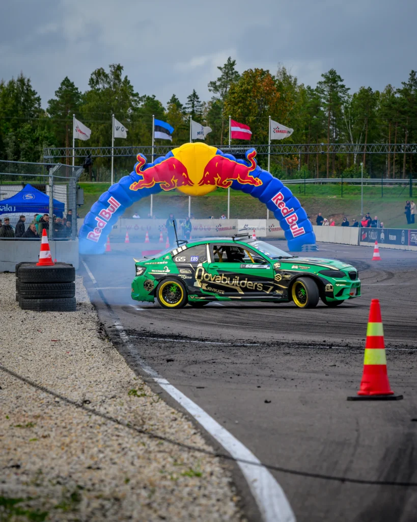 Roheline driftiauto võistluskaare ees, esiplaanil koonus ja kumer valge rajajoon.