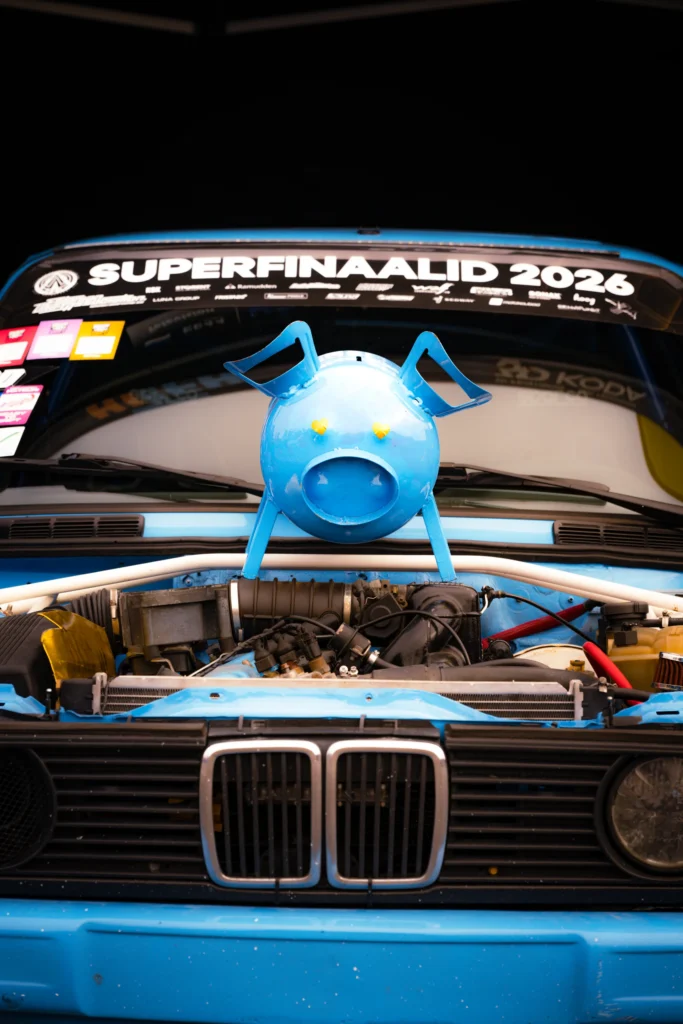 Sinine seakujuline metallkuju asetseb sinise BMW avatud mootoriruumi kohal, esiklaasil kiri „Superfinaalid 2026”.