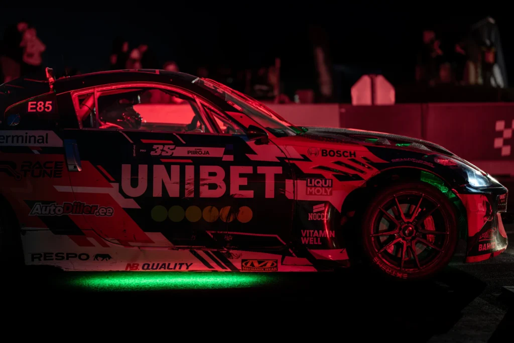 UNIBET-kirjadega punamust driftiauto külgvaates, roheline põhjavalgus ja punane valgus kerel.