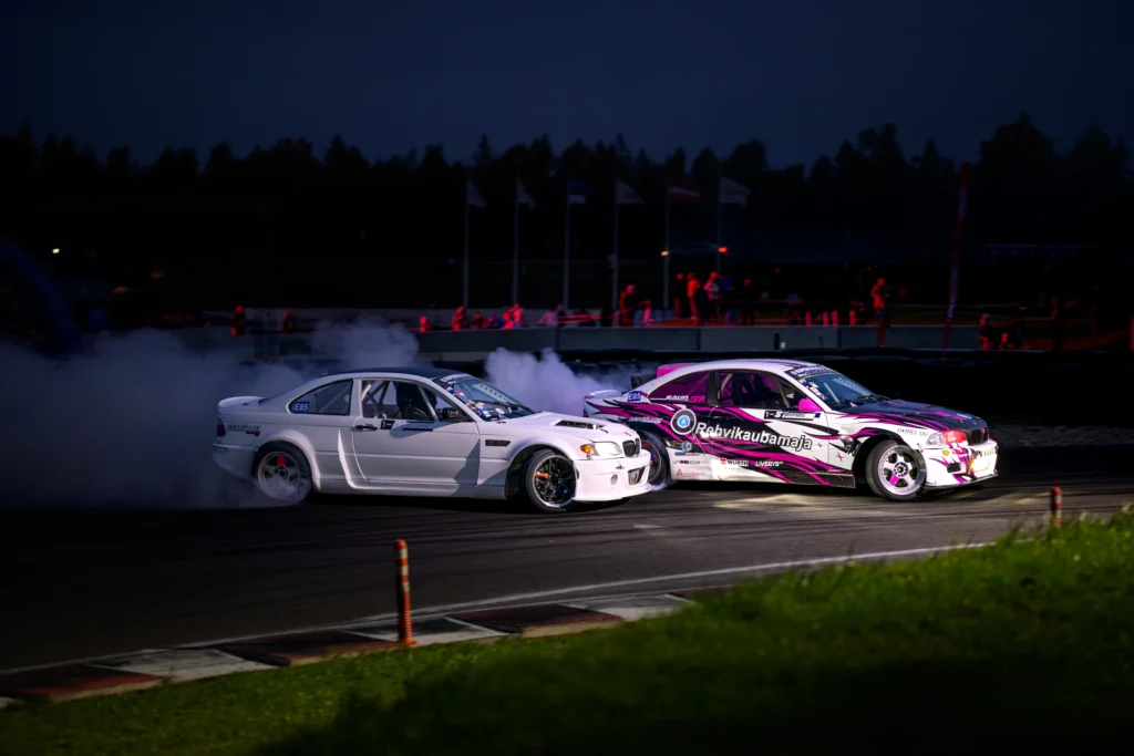 Valge ja roosamusta kujundusega driftiauto kõrvuti öisel valgustatud rajal.