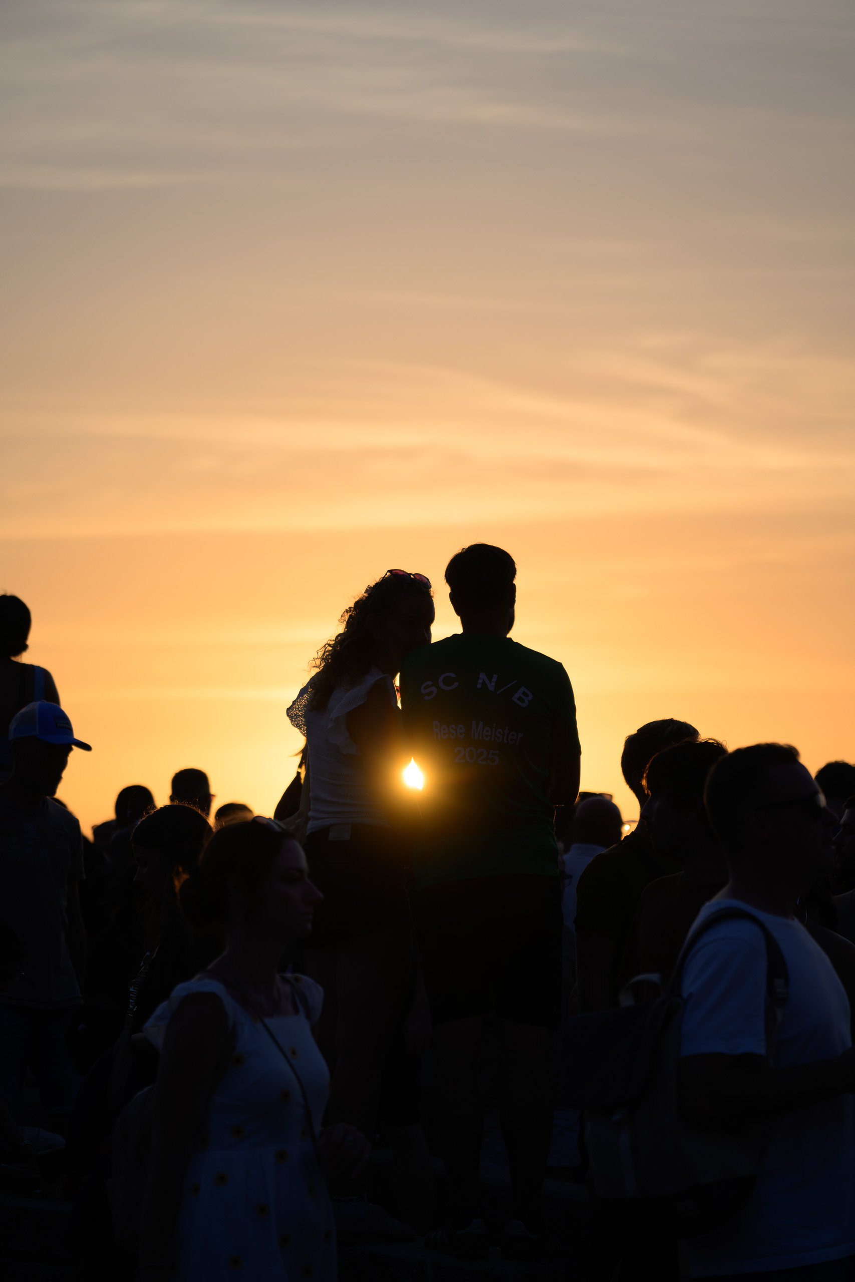 Before. Couple and crowd silhouetted against the setting sun — before applying the preset.