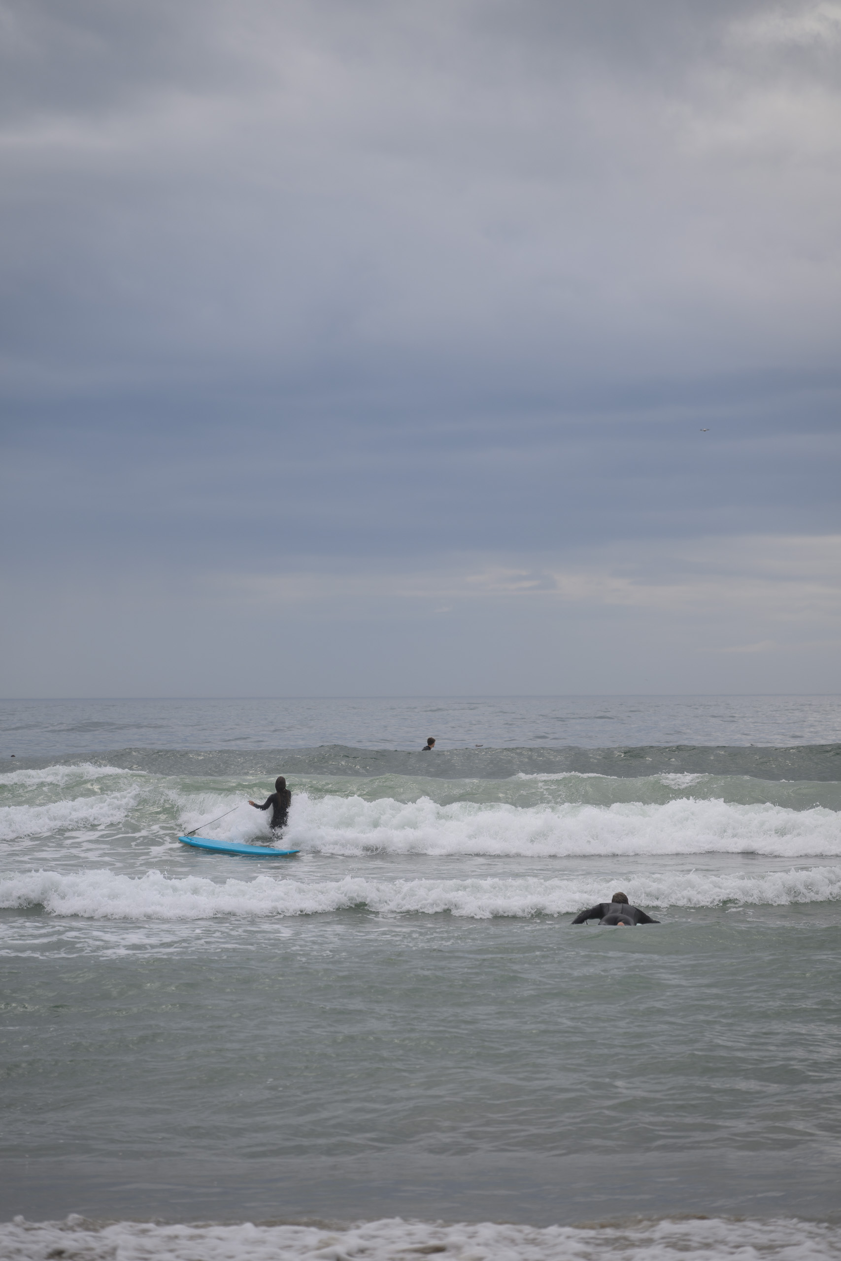 Before. Surfer on a pale wave under a darker overcast sky — before applying the preset.