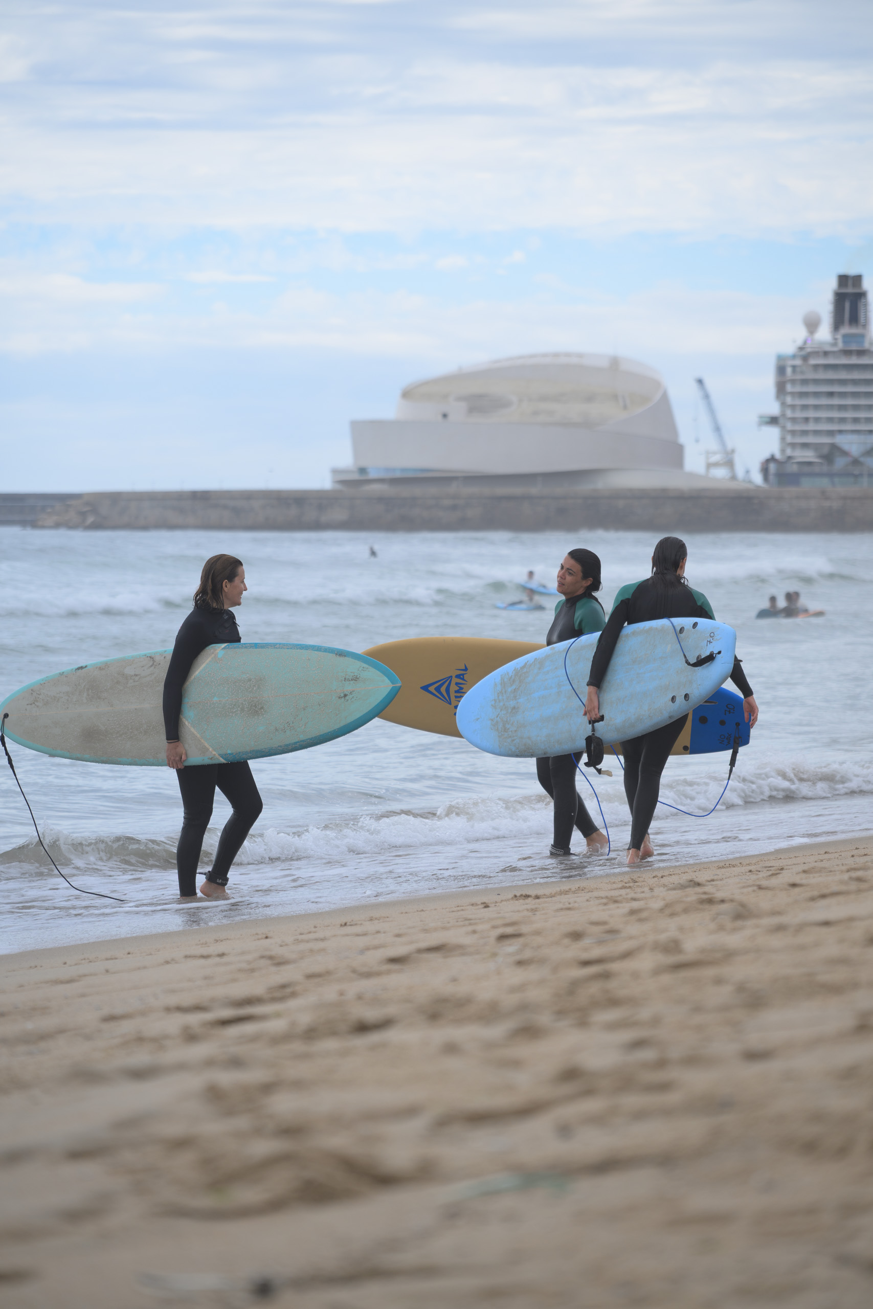 Before. Surfers carrying boards towards the sea under brighter cloud — before applying the preset.