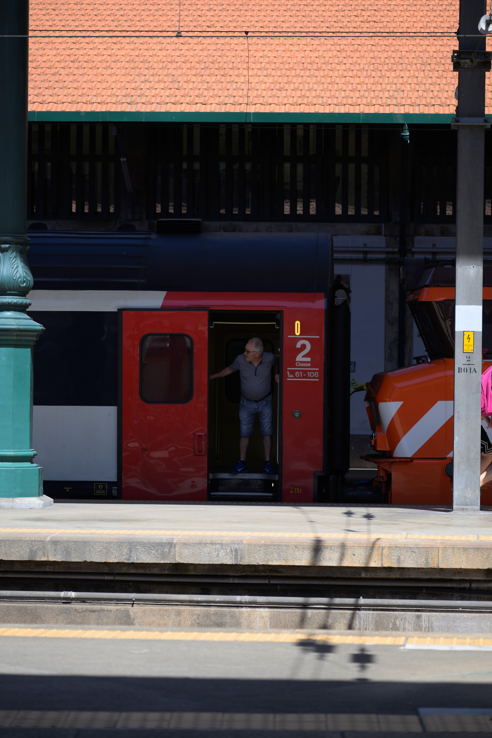 Before. Red train and passenger against deep shadows under the station roof — before applying the preset.