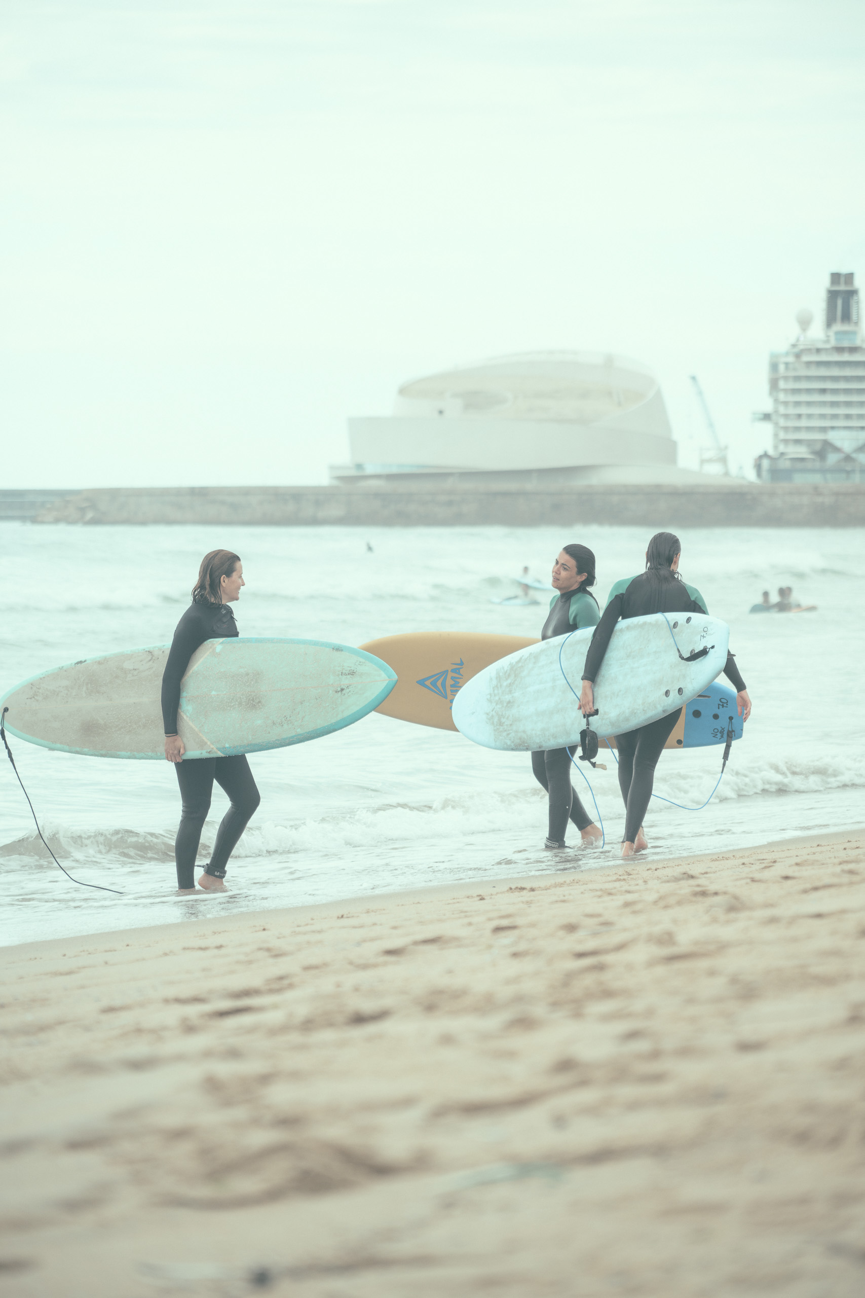 With preset. Surfers carrying boards towards the sea under brighter cloud — with the California Pastel 1968 preset.