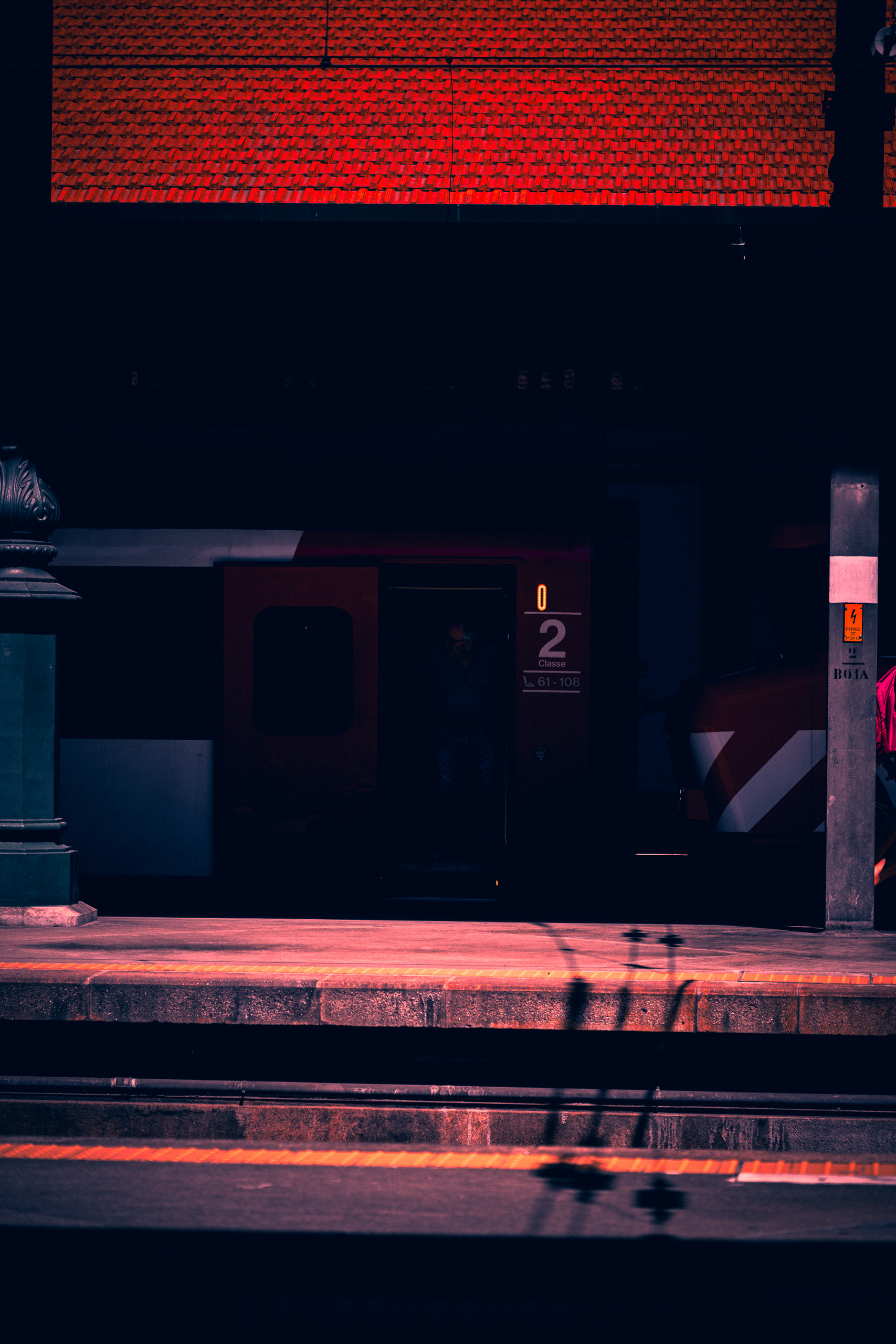 With preset. Red train and passenger against deep shadows under the station roof — with the Code Red Noir preset.