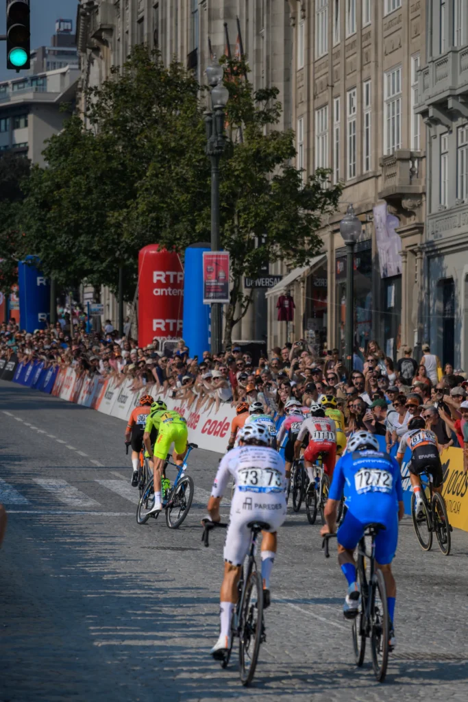 A group of cyclists rides away along a sunlit street between stone buildings in Porto.