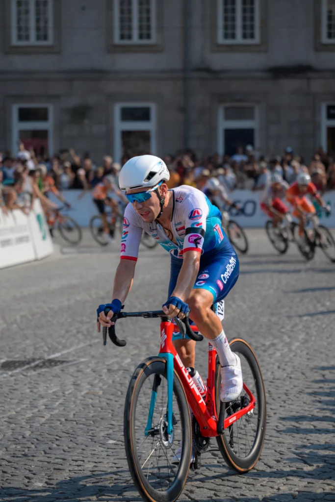 A cyclist in a white helmet and blue shorts rounds a cobbled bend on a red bicycle.