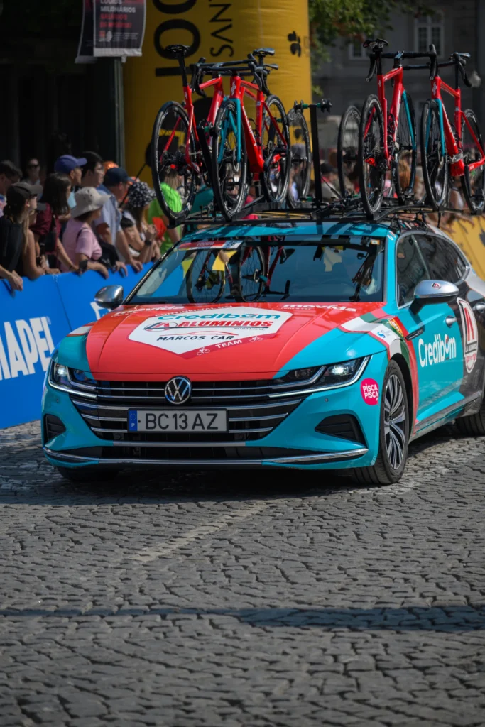 A team support car carries spare bicycles on its roof on a cobbled street in Porto.