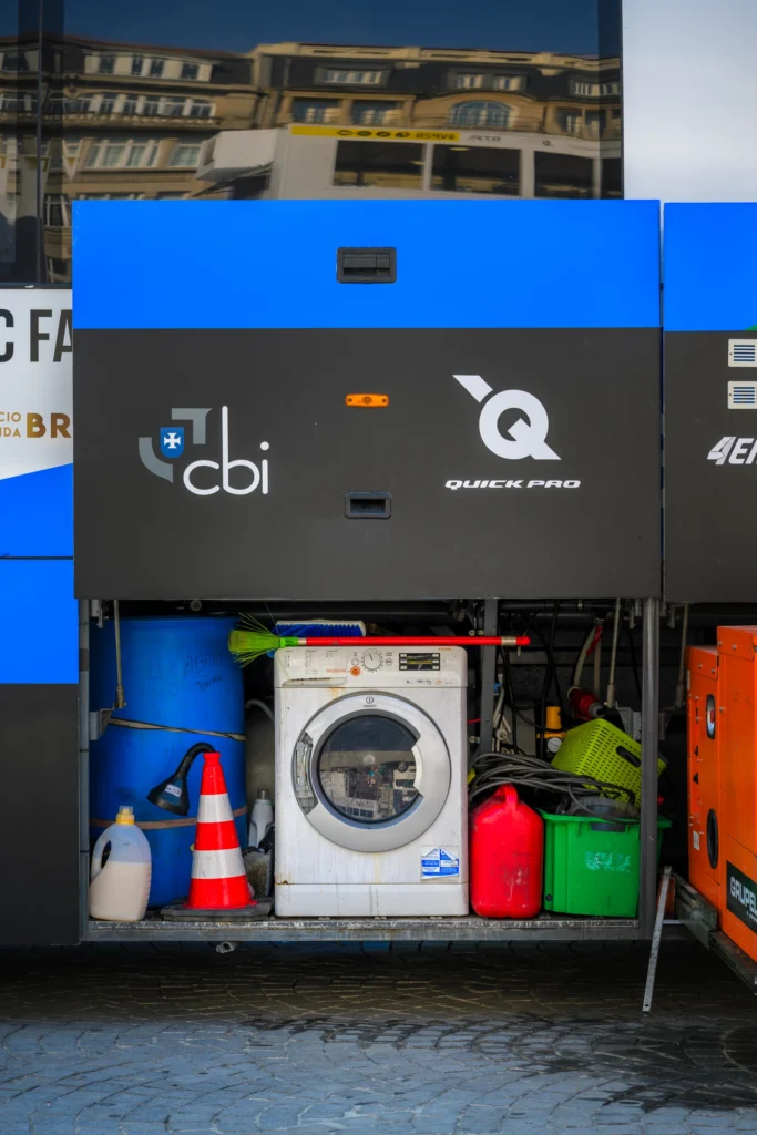 An open compartment in a team bus holds a washing machine, canisters and equipment.