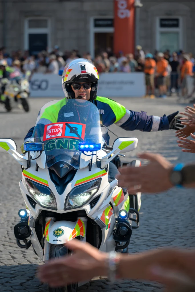 A police motorcycle escort reaches a hand towards spectators beside the course.