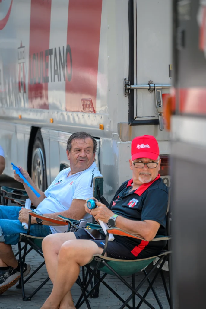 Two men sit in folding chairs beside a truck at the race venue.