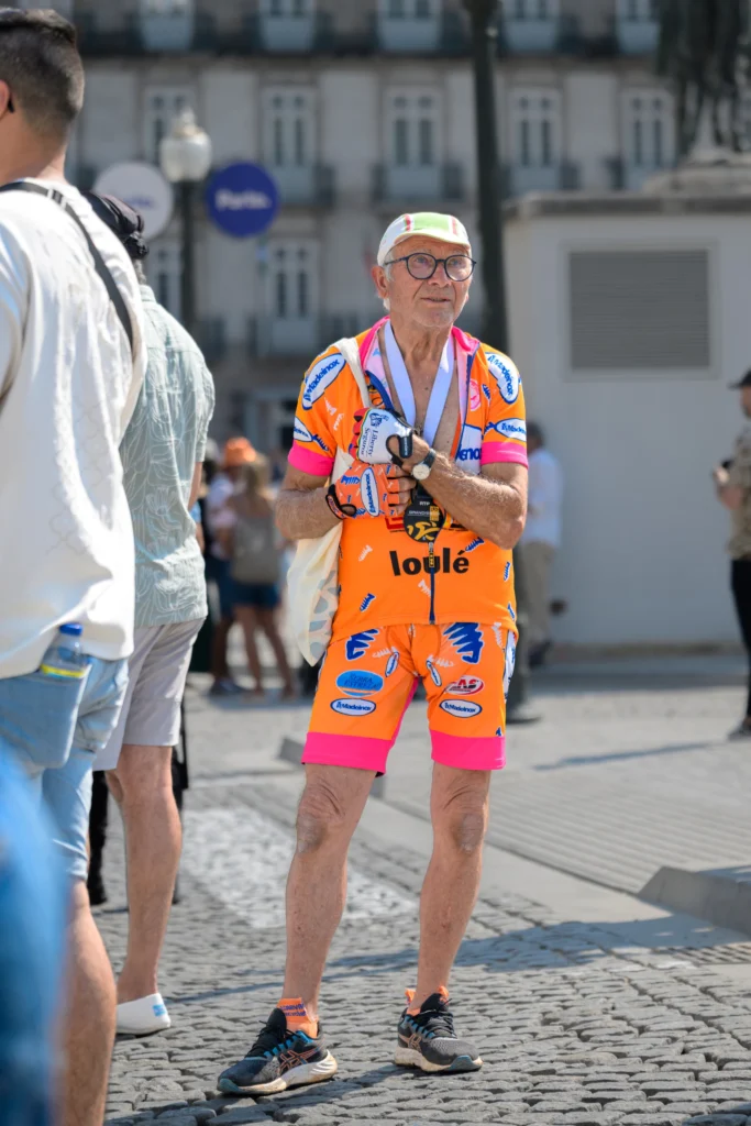 A man in vivid orange and pink cycling kit stands at the race venue in Porto.