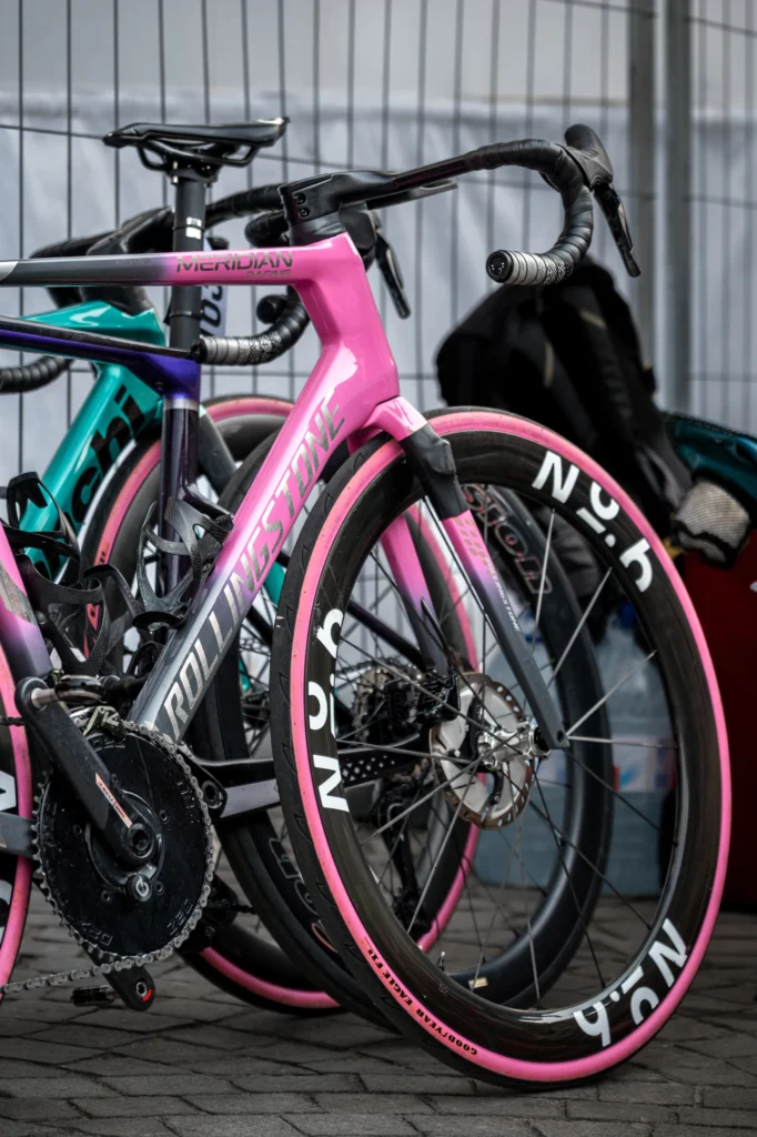 Spare bicycles with pink and green frames stand beside team equipment.