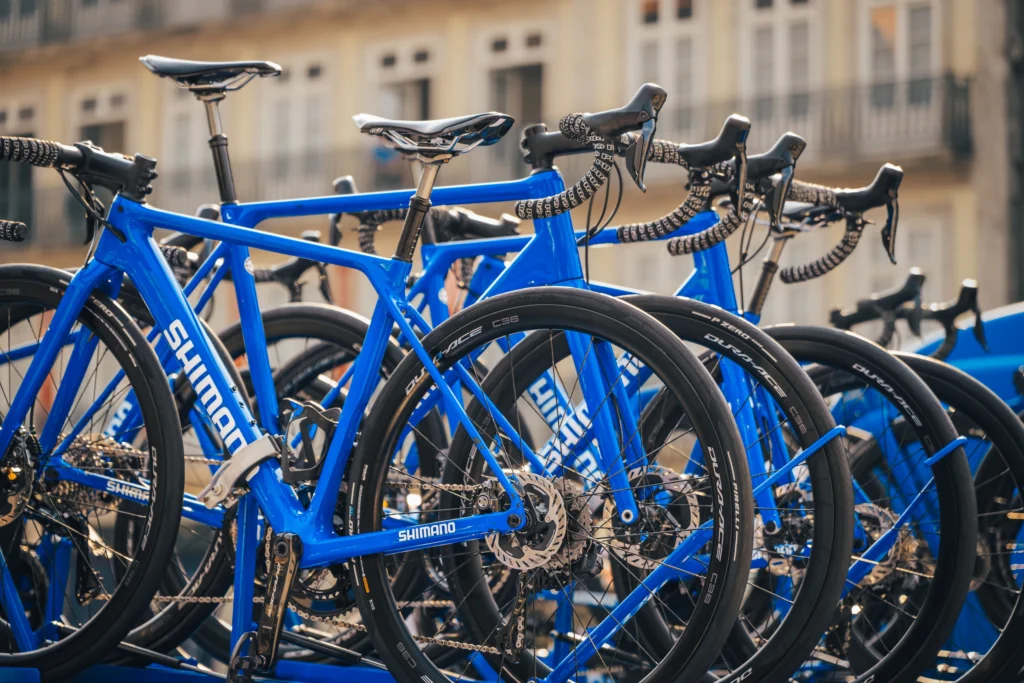 Blue road bicycles are lined up closely on the roof of a technical support car.