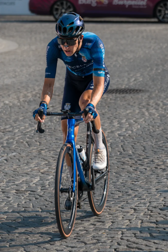 A cyclist in blue racing kit looks ahead while riding over uneven cobbles.
