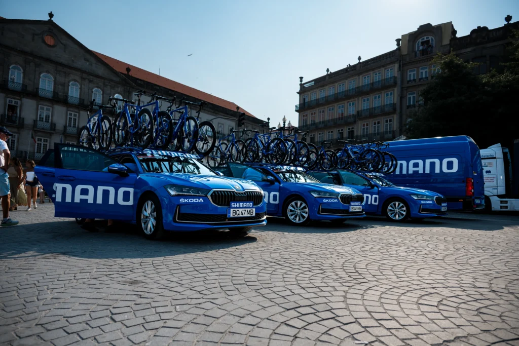 Blue Shimano technical support cars with roof-mounted bicycles on a square in Porto.