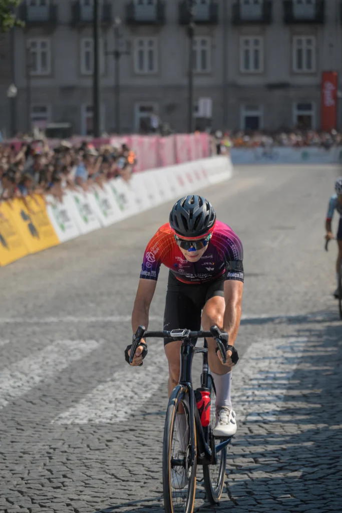 A cyclist in a red and dark jersey rides head down over the cobbles.