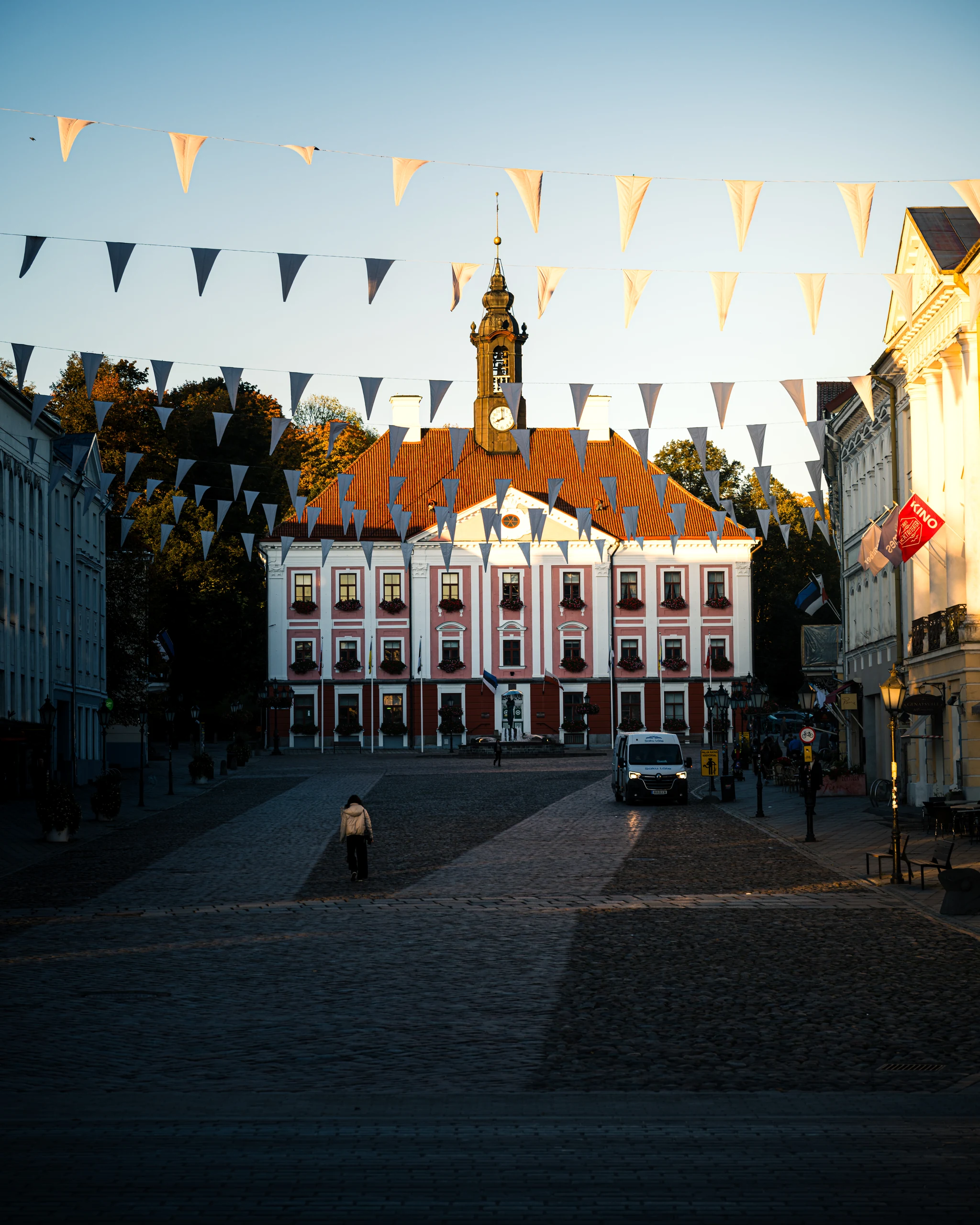 The pink facade of Tartu Town Hall in morning light, with pennants above the square and long shadows in the foreground.