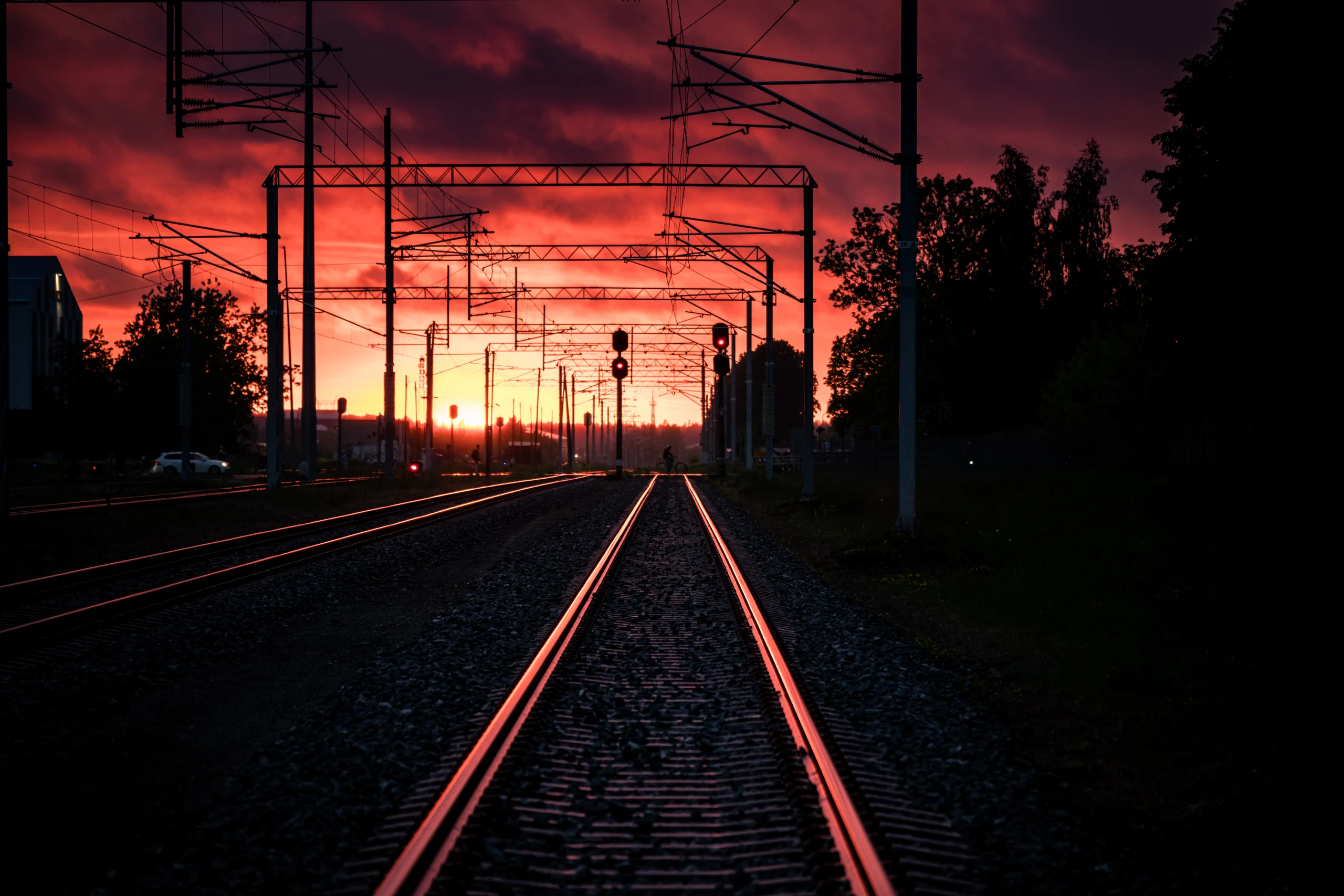 Glowing rail edges and overhead line masts recede towards an orange-red sunset.